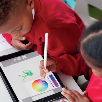 Two primary school children in school uniforms working around a tablet. One child is selecting a colour using a stylus in a drawing app.